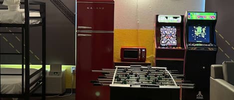 A room with a foosball table, a red Galanz refrigerator, a microwave, and two Atari gaming consoles.