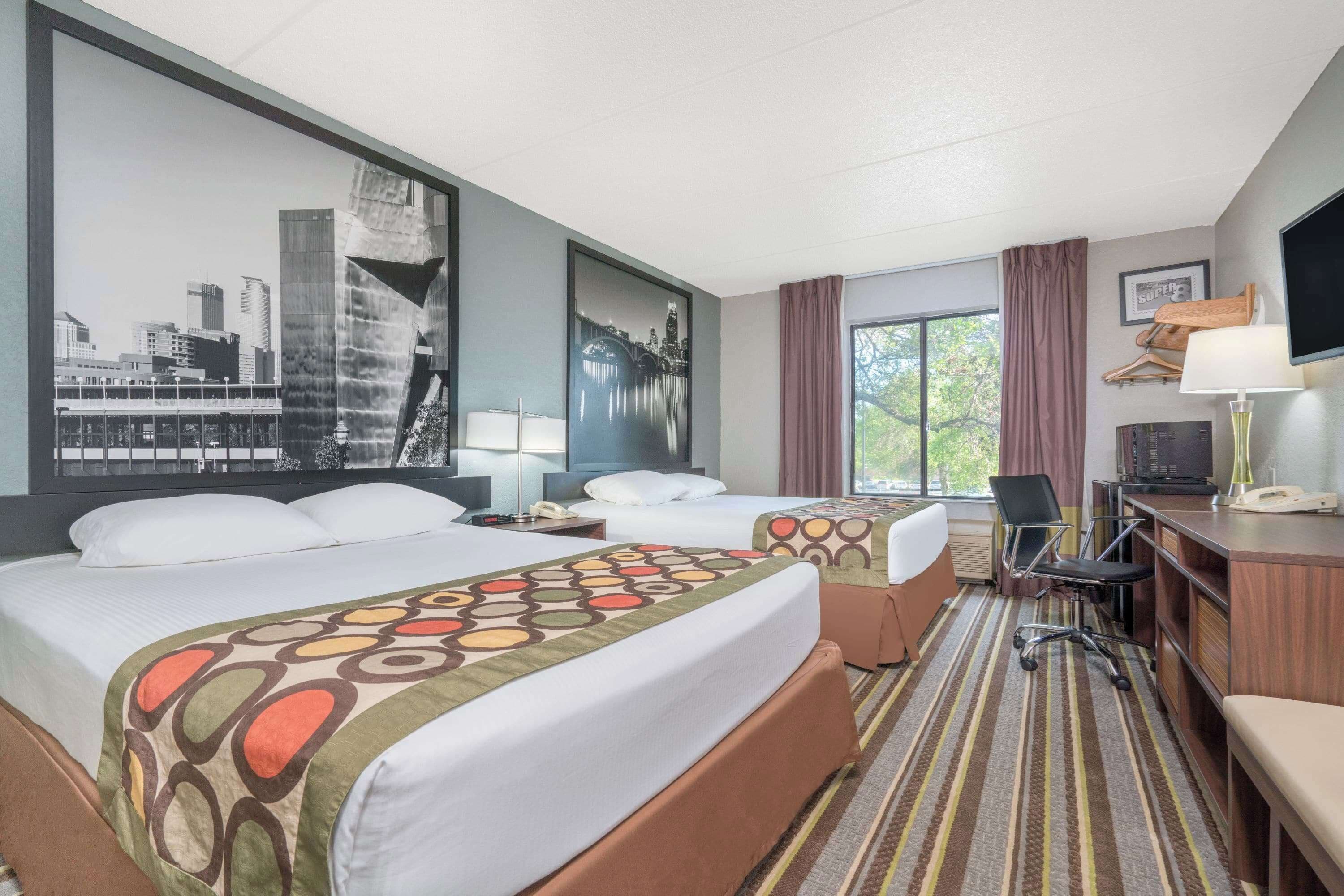 Una habitación de hotel con dos camas, un escritorio, una silla, un televisor y una ventana con cortinas.
