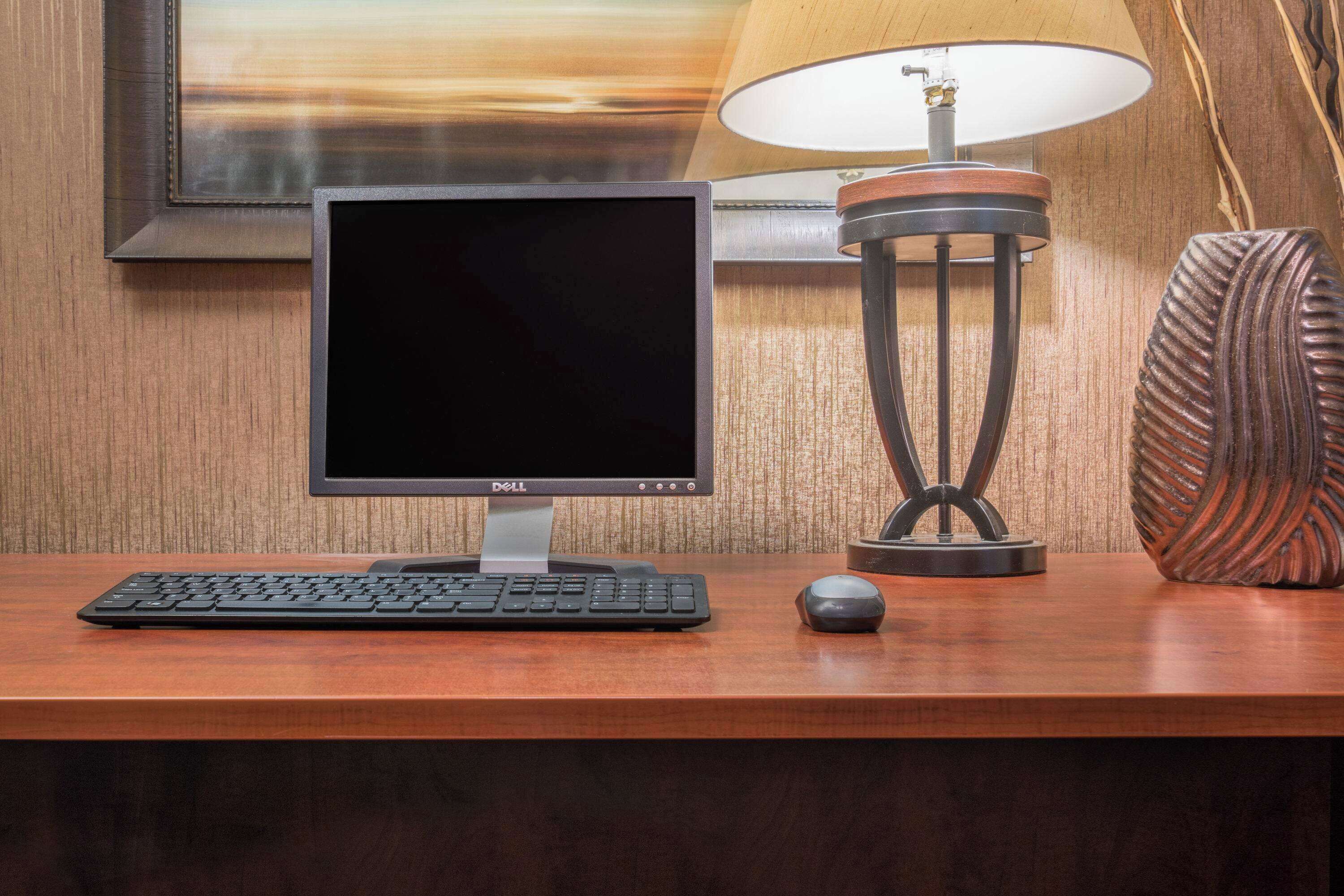 Een bureau met een Dell monitor, toetsenbord en muis, een lamp en een decoratieve vaas.