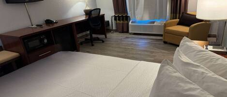 Una habitación de hotel con una cama, un escritorio con silla, televisión, aire acondicionado y lámpara.