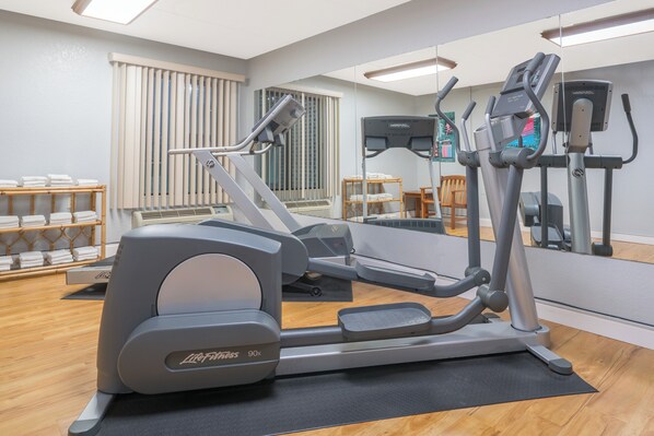 Un gimnasio con equipo de ejercicio, un muro espejado y piso de madera.
