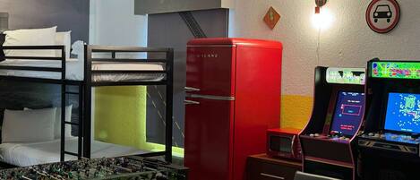 A room with bunk beds, a red refrigerator, a foosball table, and arcade games.