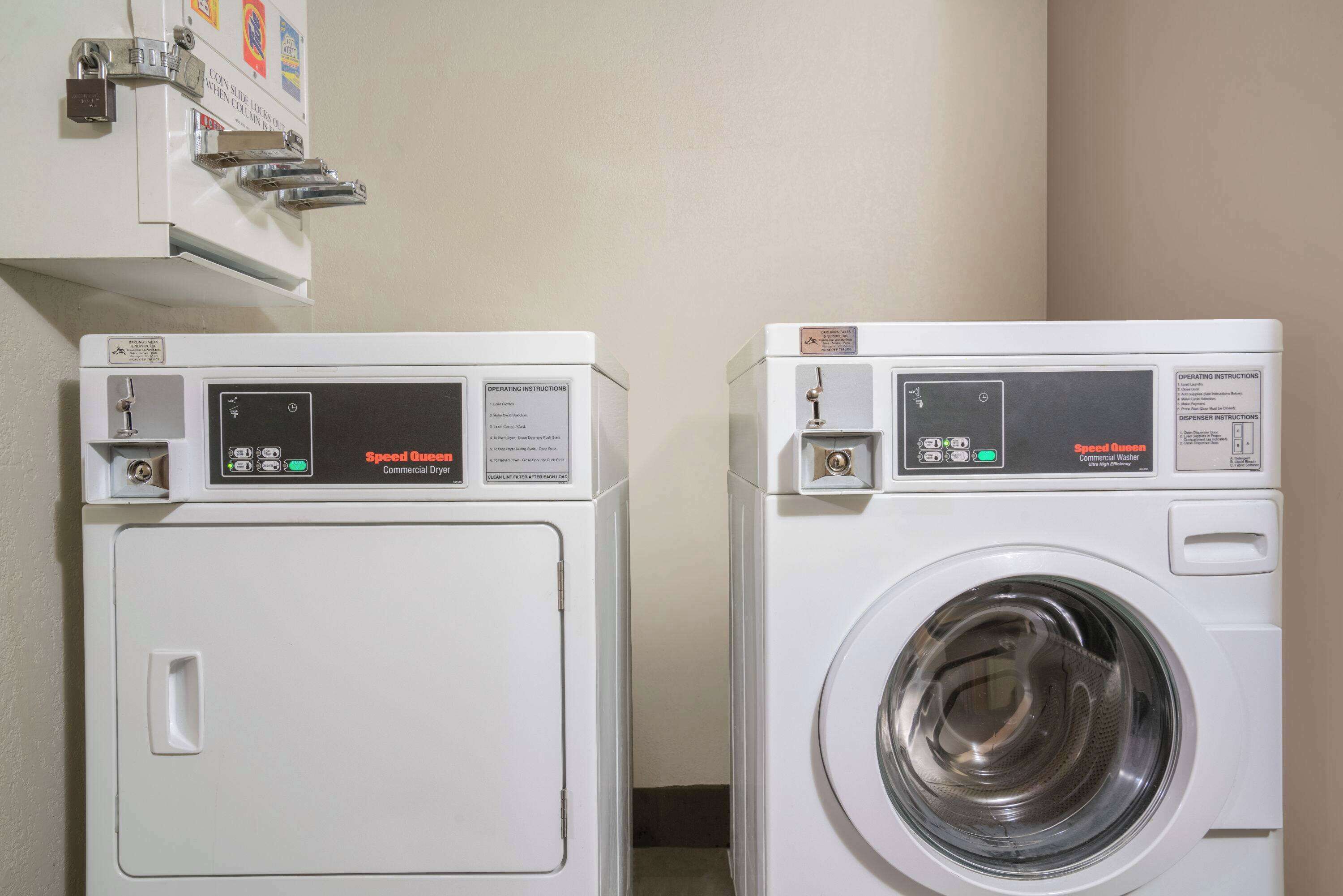 Two front-loading commercial washers in a laundry room with operating instructions and safety labels.