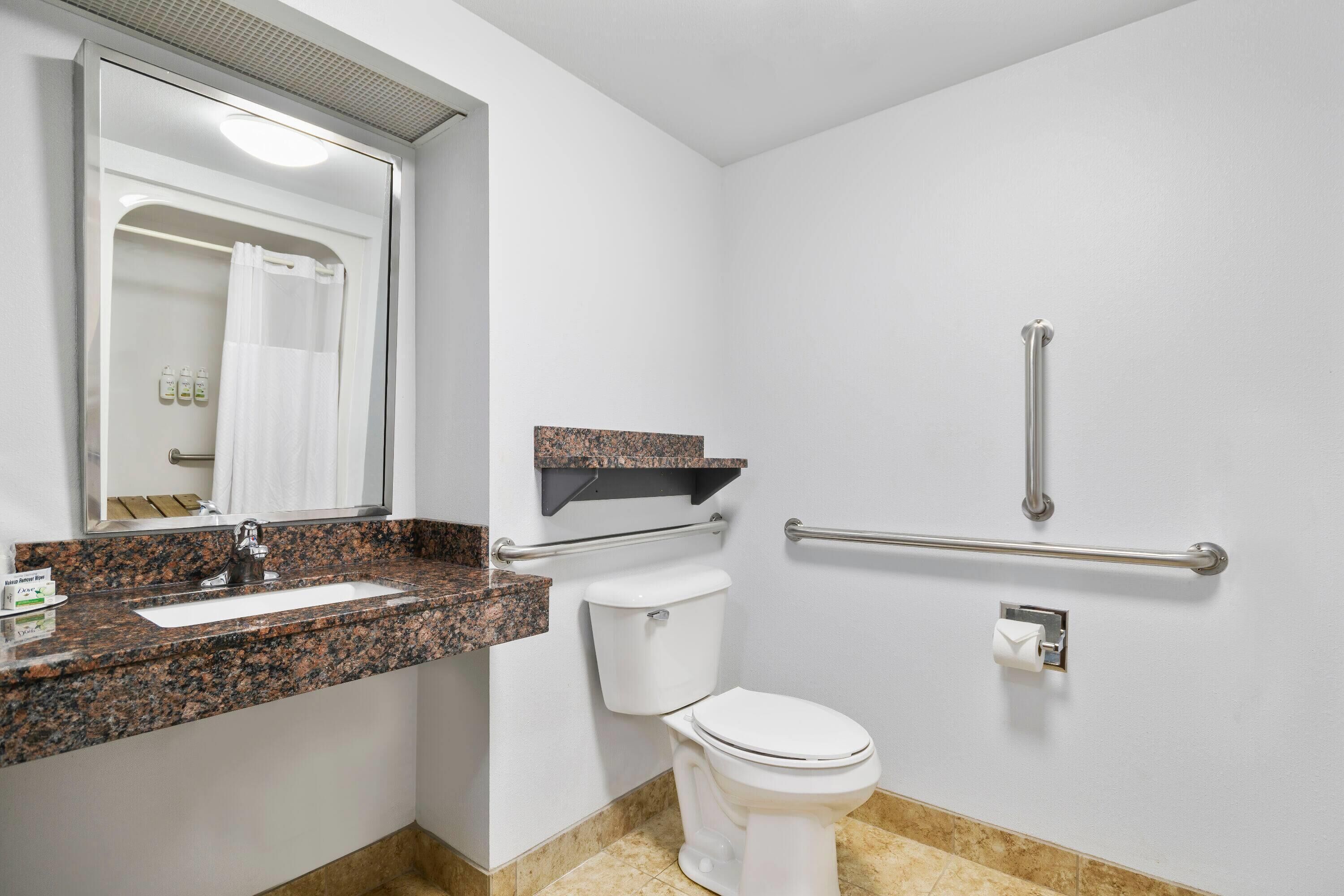 A bathroom with a white toilet, a granite countertop sink, a mirror, a towel rack, and a grab bar.
