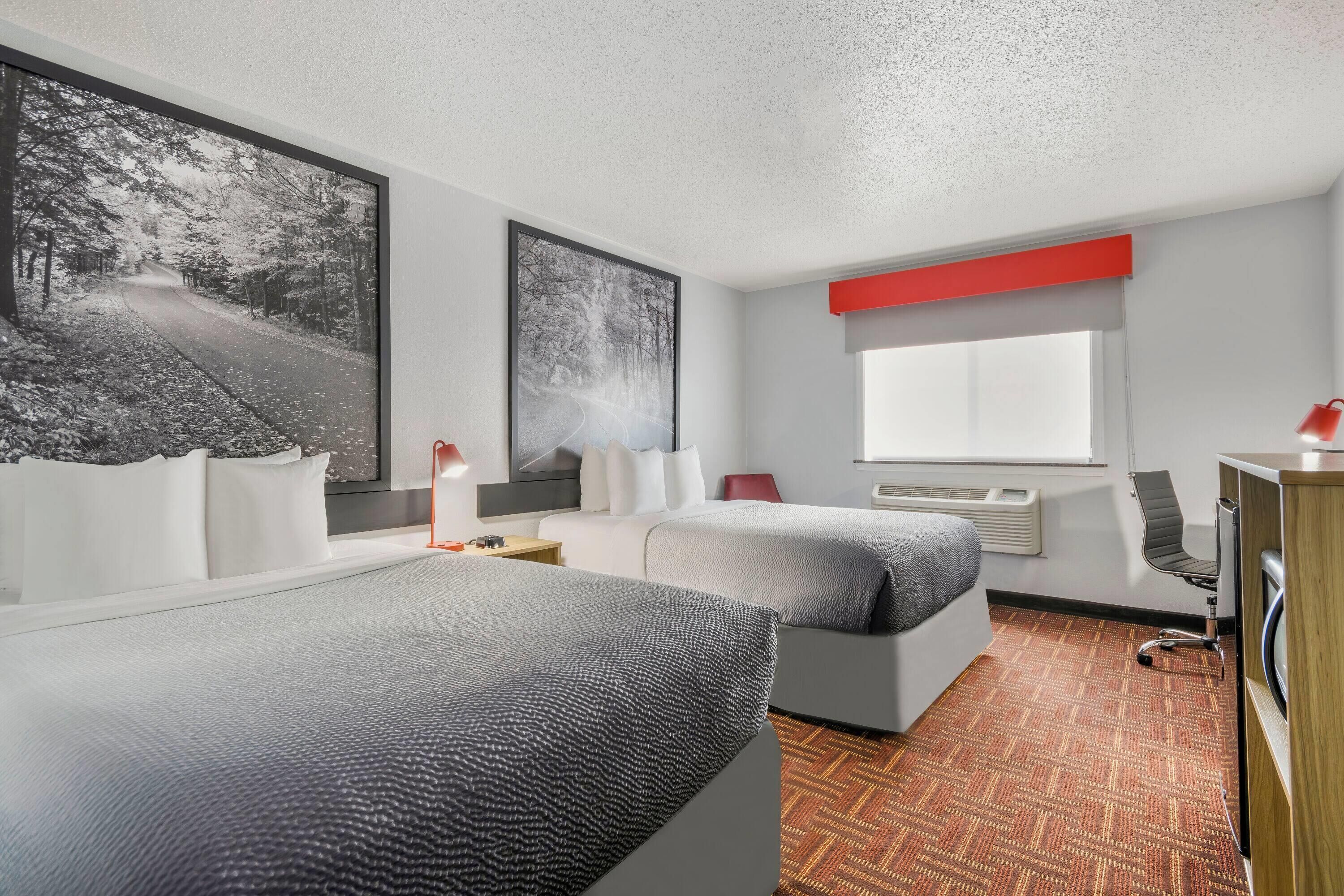 A modern hotel room with two beds, a large window, and a view of a road.