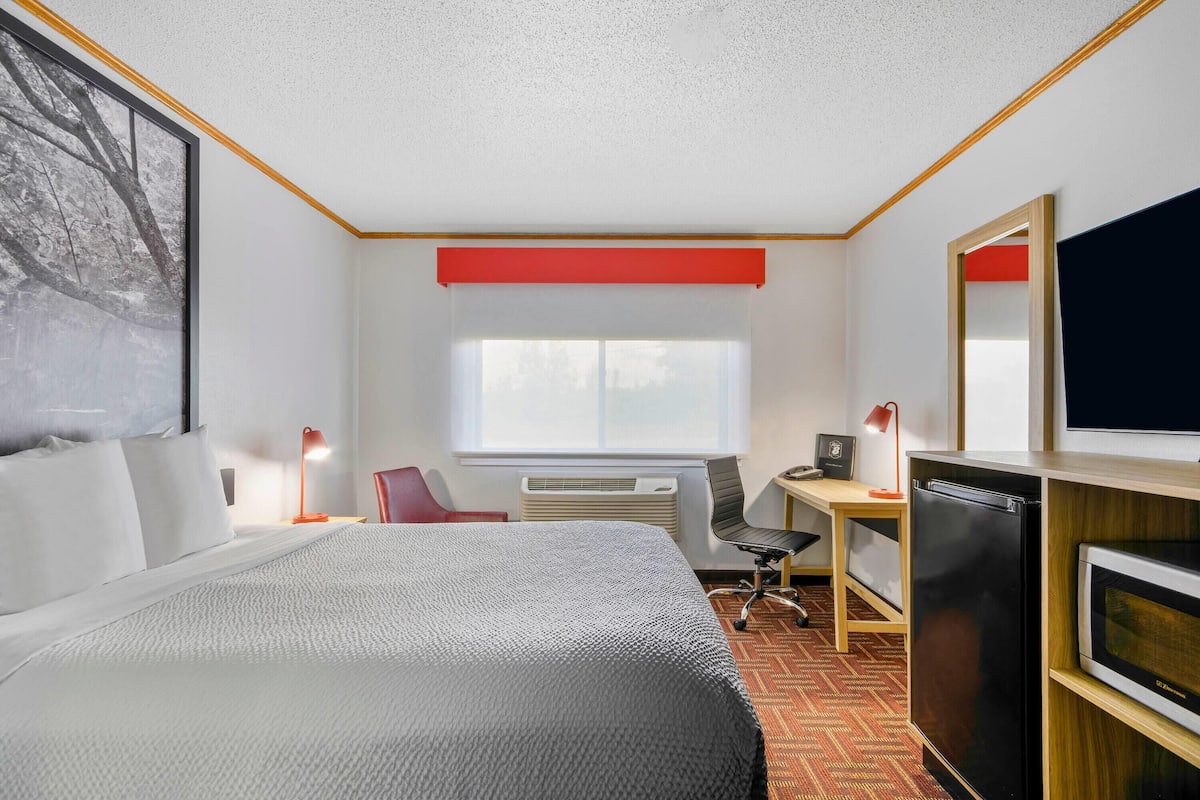 Une chambre d’hôtel équipée d’un lit, d’un bureau, d’une chaise, d’un réfrigérateur et d’une grande fenêtre.