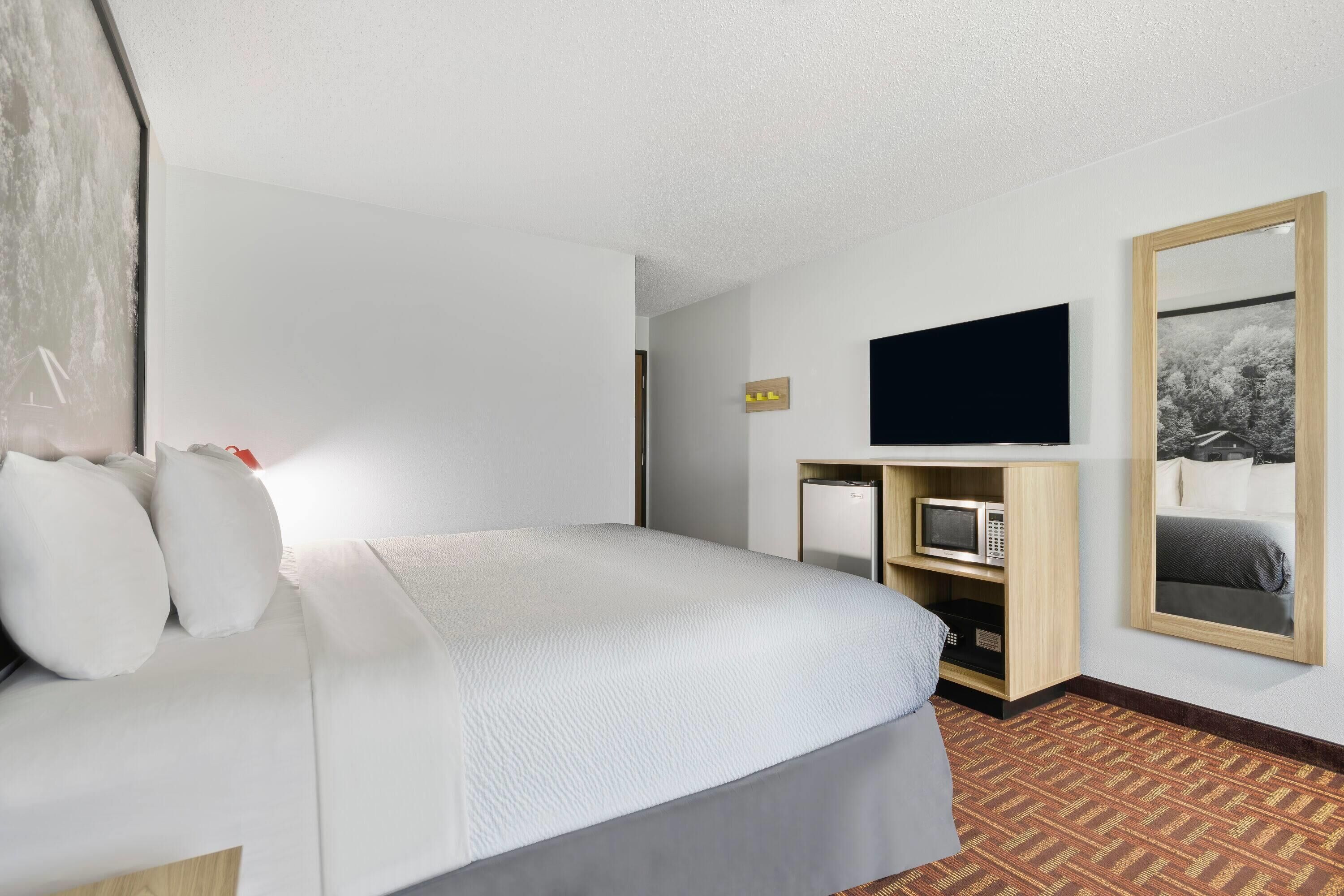 Camera d'albergo con un letto, una televisione a schermo piatto montata a parete, un piccolo frigorifero e uno specchio.