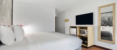 Camera d'albergo con un letto, una televisione a schermo piatto montata a parete, un piccolo frigorifero e uno specchio.
