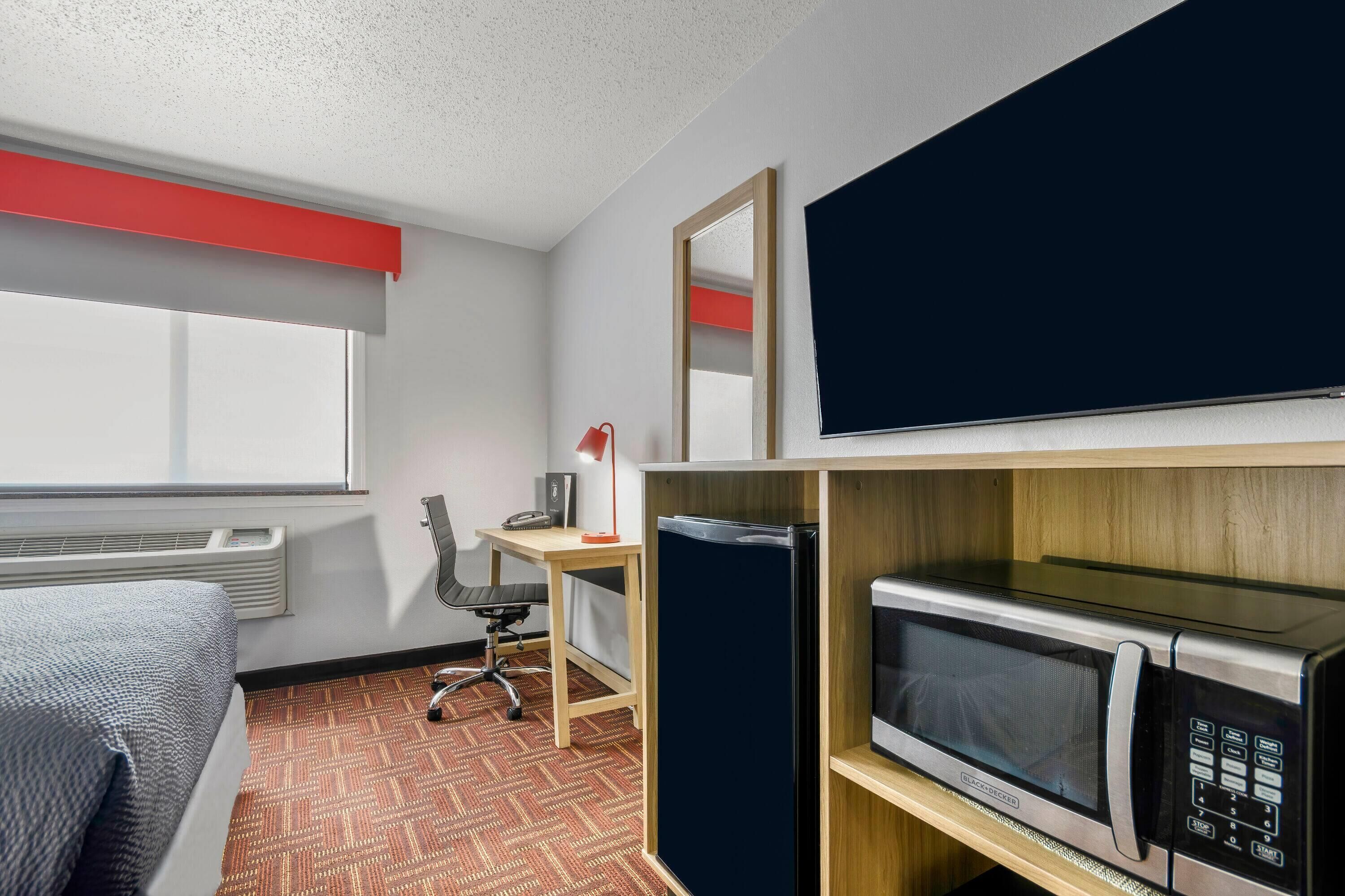 A hotel room with a bed, a desk, a chair, a microwave, and a window.