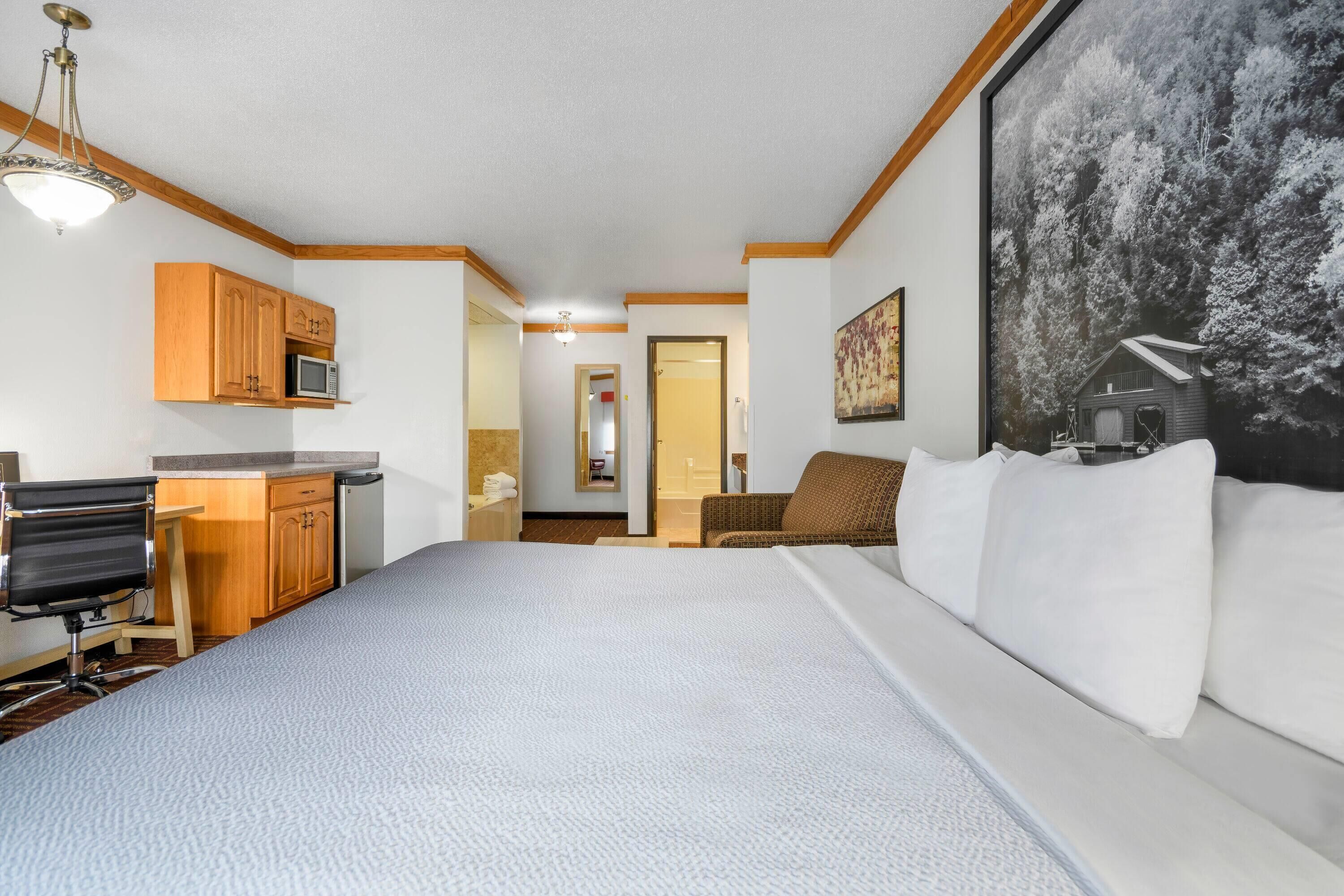 A hotel room with a large bed, a desk with a chair, a microwave, and a painting on the wall.