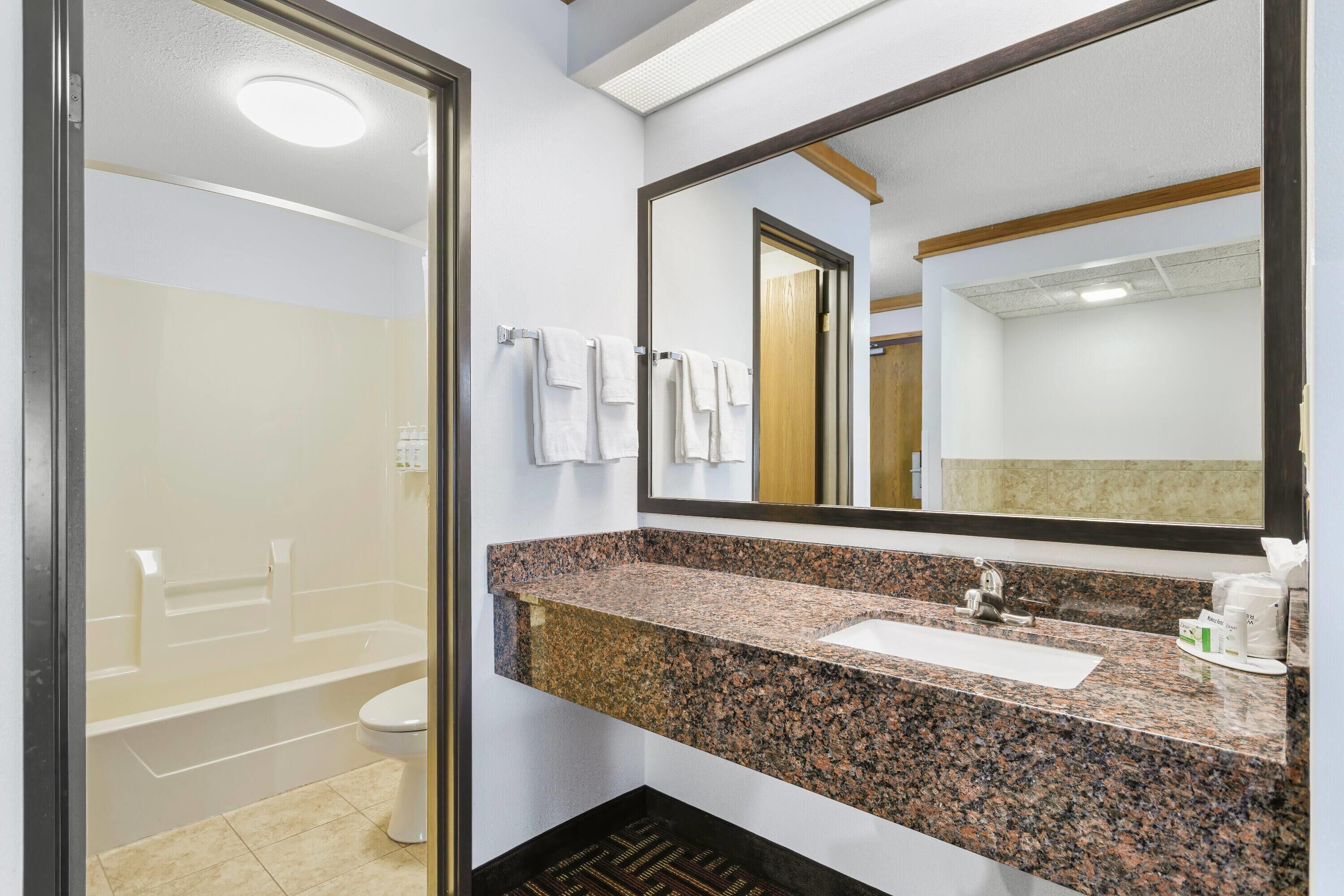 A modern bathroom with a granite countertop, a sink, and a large mirror.