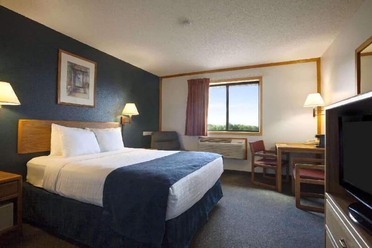 Une chambre d’hôtel équipée d’un lit, d’un bureau, d’une chaise, d’une télévision et d’une fenêtre avec des rideaux.