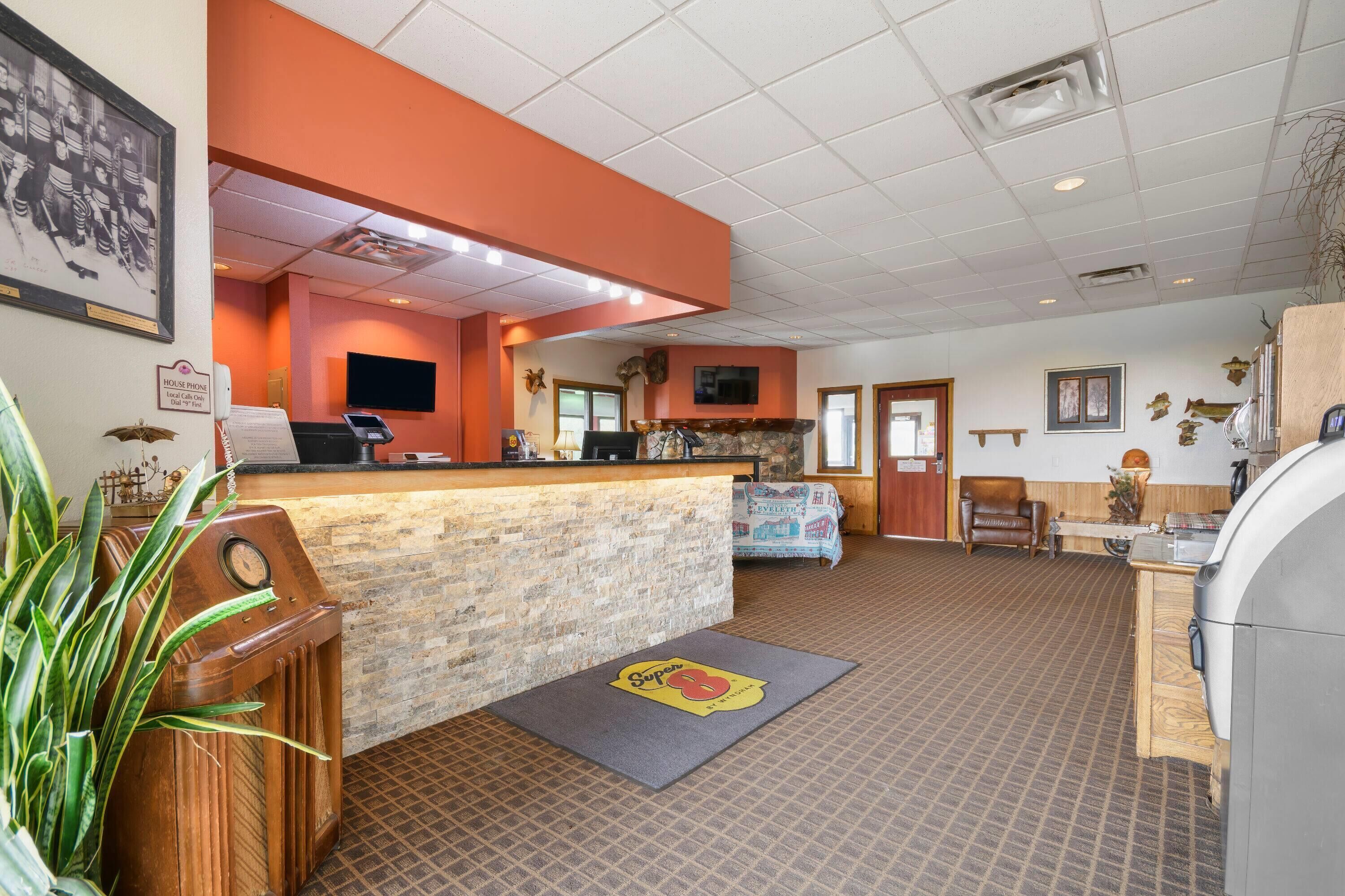 A hotel lobby with a reception desk, a clock, a television, and a fireplace.