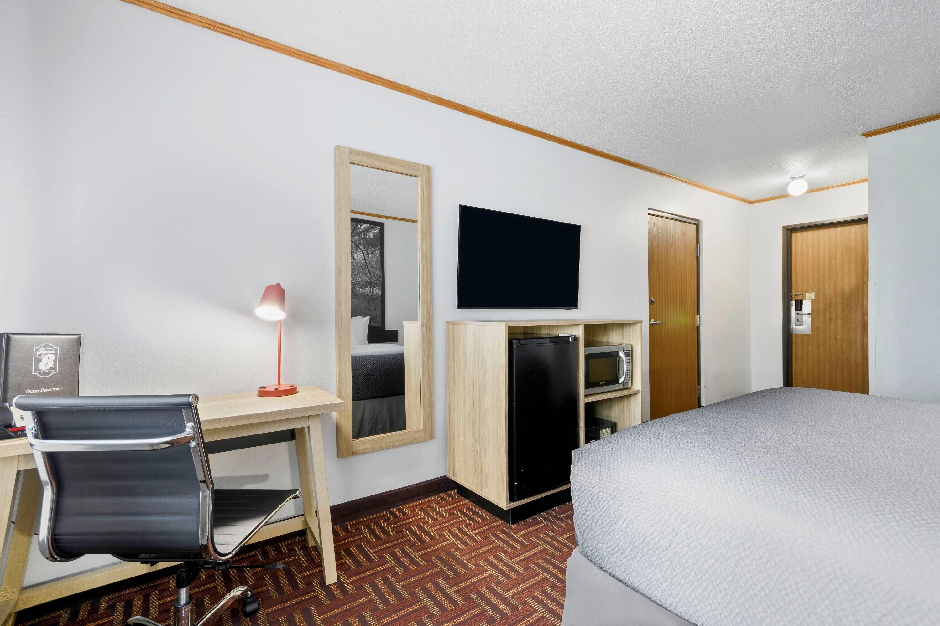 A hotel room with a bed, desk, chair, TV, and a wardrobe.