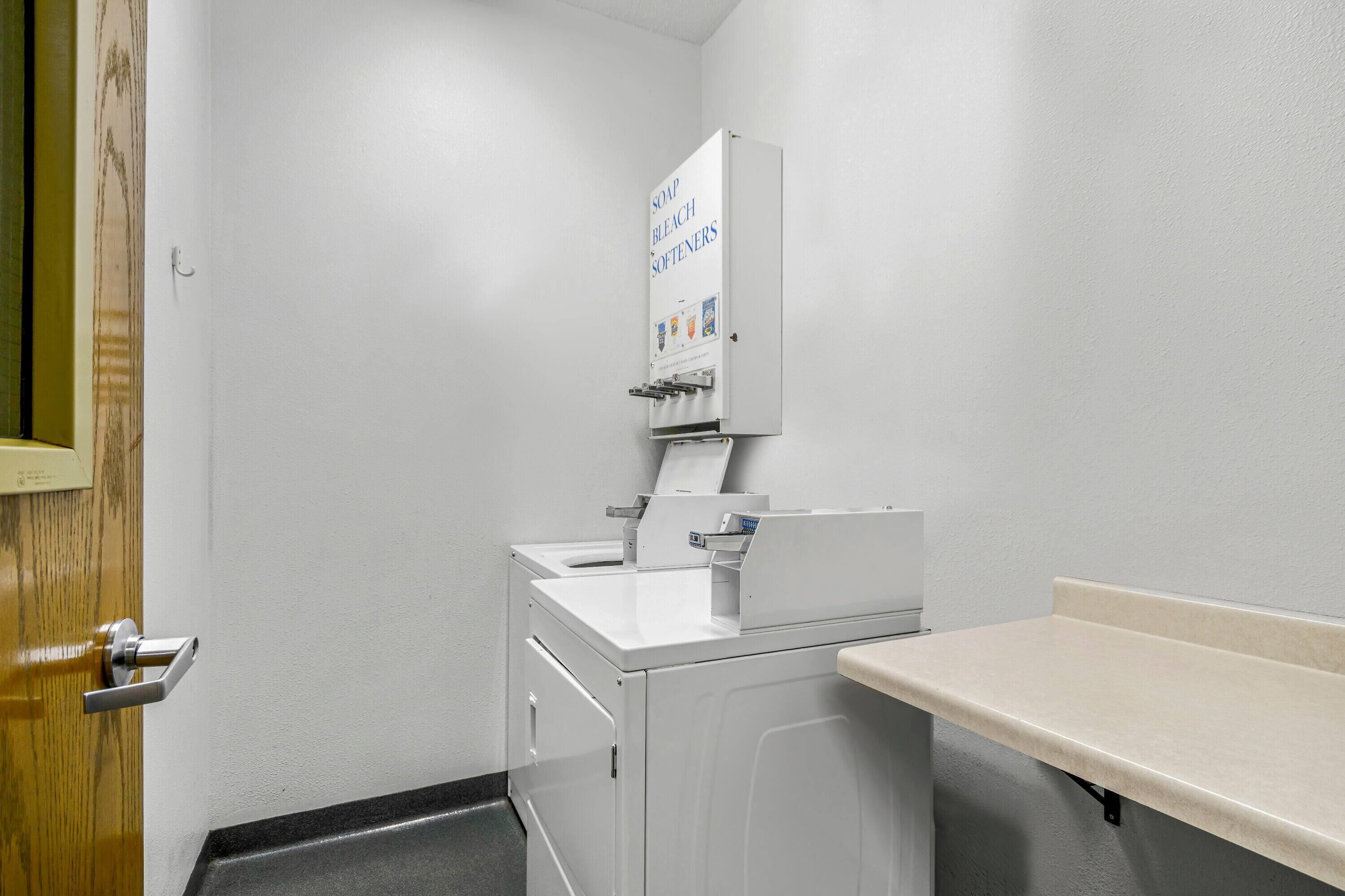 A small laundry room with a white washing machine, a sink, and a soap dispenser.