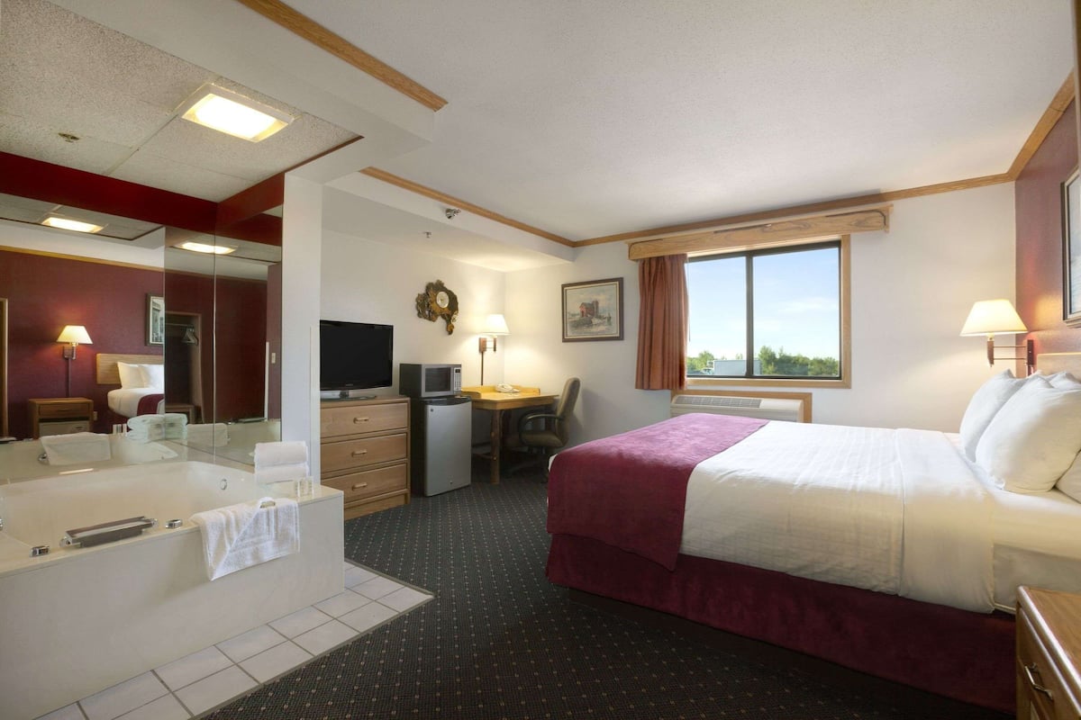 Une chambre d’hôtel avec un grand lit, un bureau avec un ordinateur, une télévision, une salle de bain avec une baignoire et une fenêtre donnant sur un beau paysage.