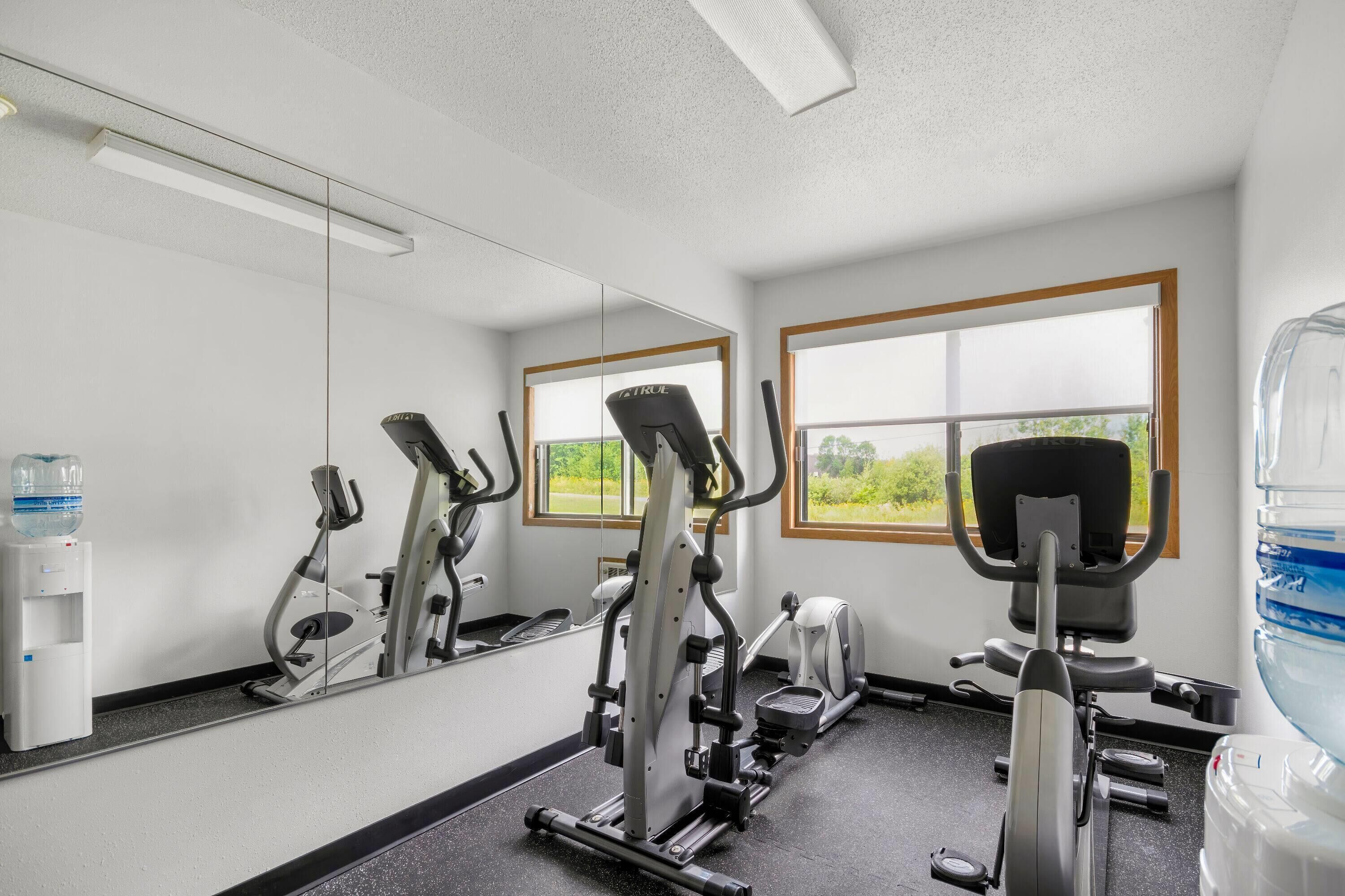 Ett gym med träningsutrustning, en vattenautomat och en stor spegel.