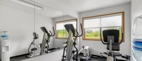 Ett gym med träningsutrustning, en vattenautomat och en stor spegel.
