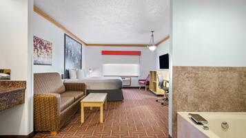 A hotel room with a bed, a sofa, a small table, a desk, a chair, a TV, and a bathroom with a bathtub.