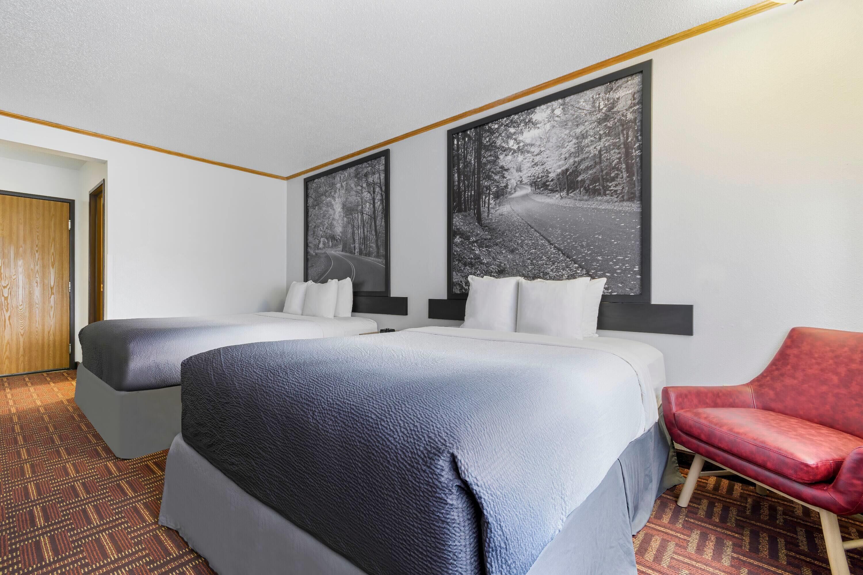 Une chambre d’hôtel avec deux lits, un fauteuil rouge et de grandes images encadrées accrochées au mur.