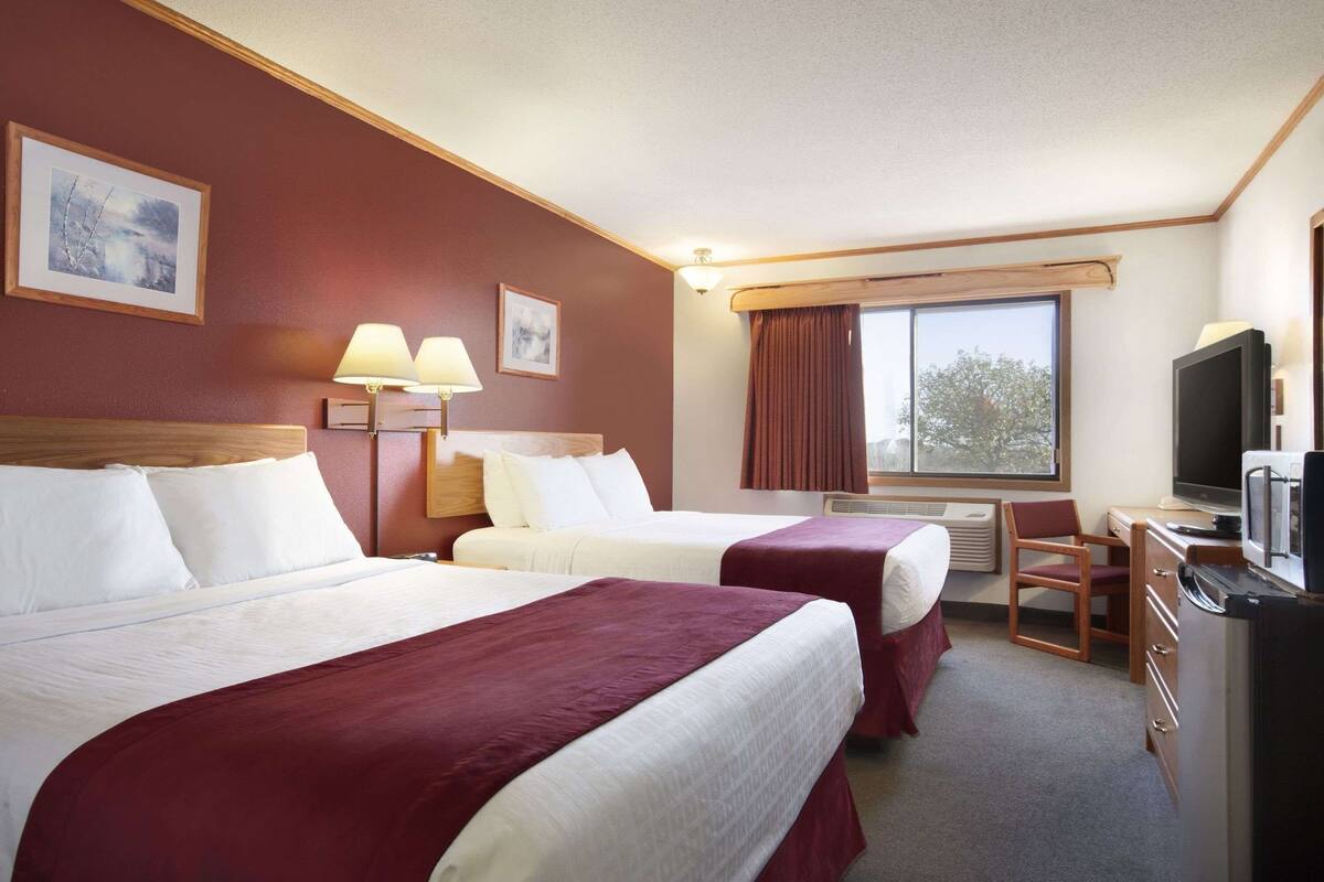 Une chambre d’hôtel avec deux lits, un bureau, une télévision et une fenêtre avec des rideaux.