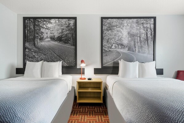 Habitación de hotel con dos camas, una mesita de noche con lámpara y dos grandes cuadros enmarcados de un camino forestal.