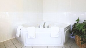 A bathroom with a white bathtub, two faucets, and a white tiled wall. - Coratel Inn & Suites By Jasper Northfield (Northfield)