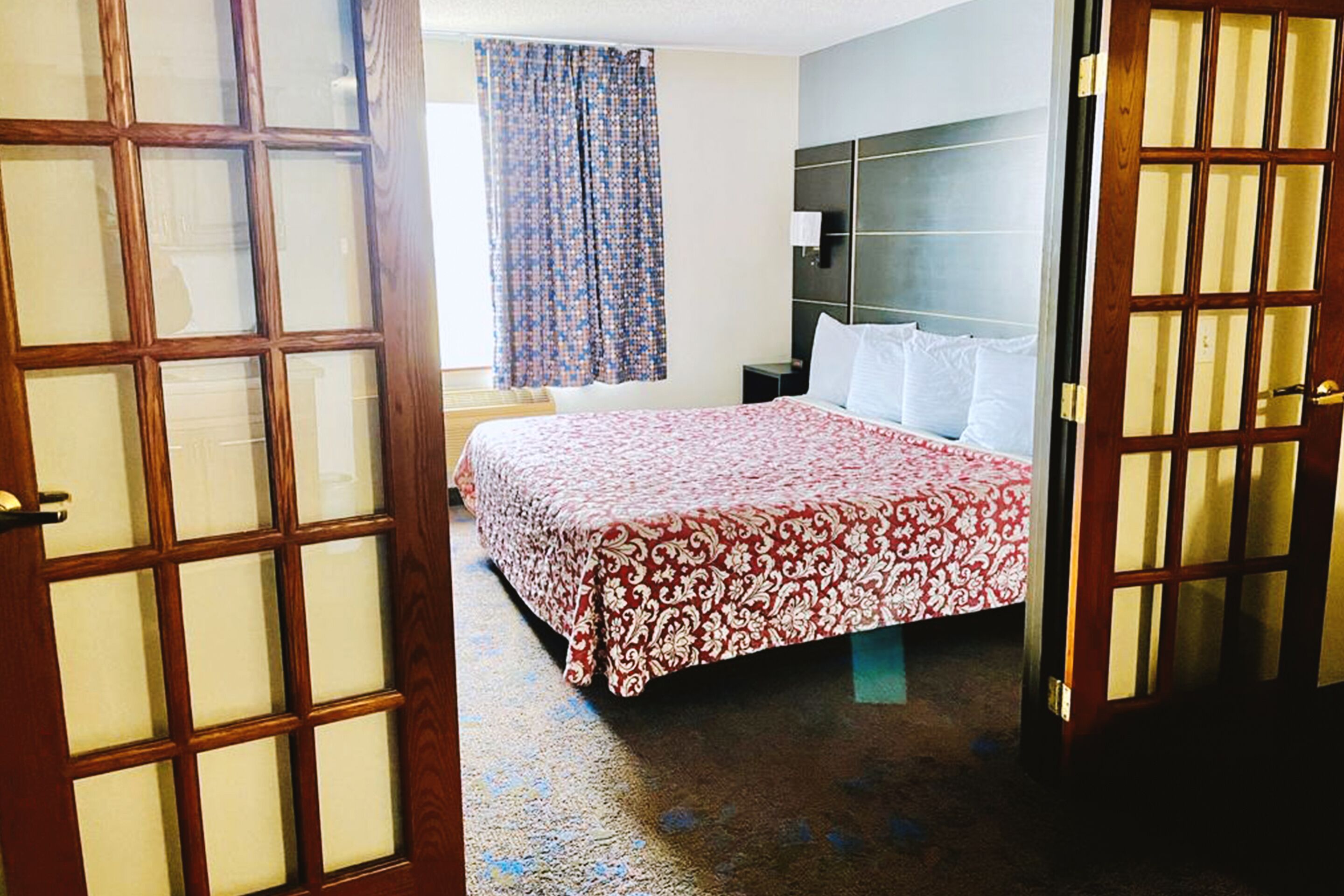 A hotel room with a large bed, a nightstand, a lamp, and a window with curtains.