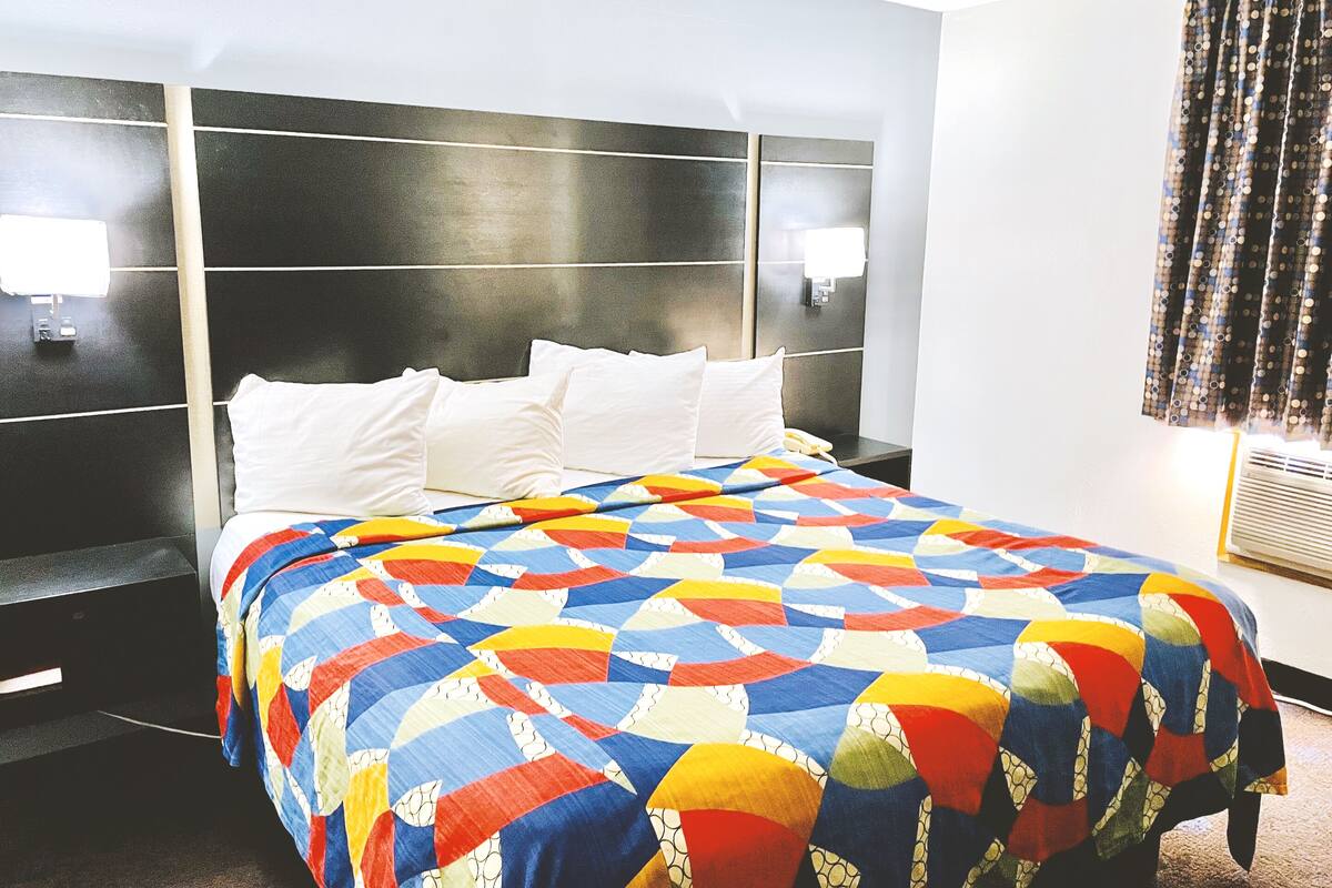 A hotel room with a large bed, a headboard, two bedside lamps, and a window with curtains.