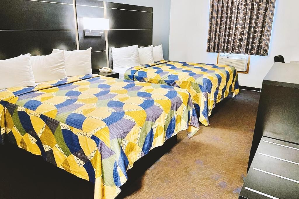 A hotel room with two beds, a desk, and a window with curtains.