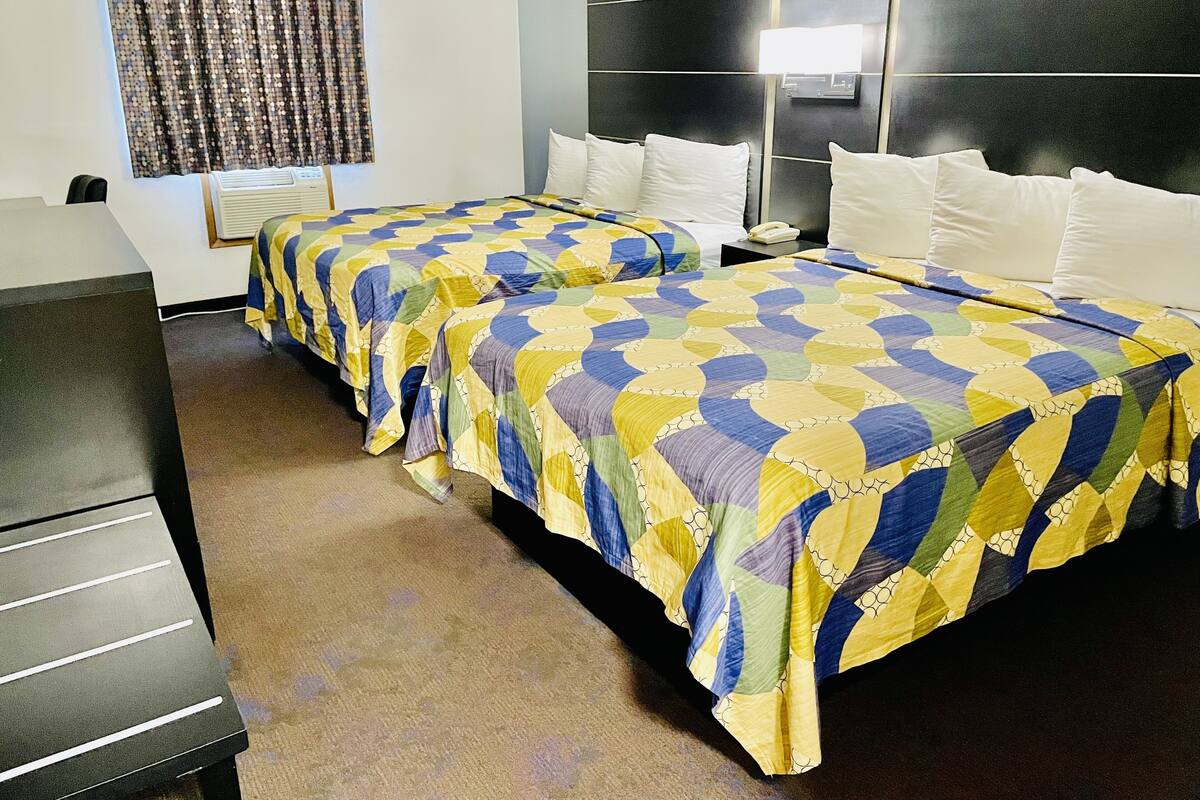 A hotel room with two beds, a desk, and a window with curtains.