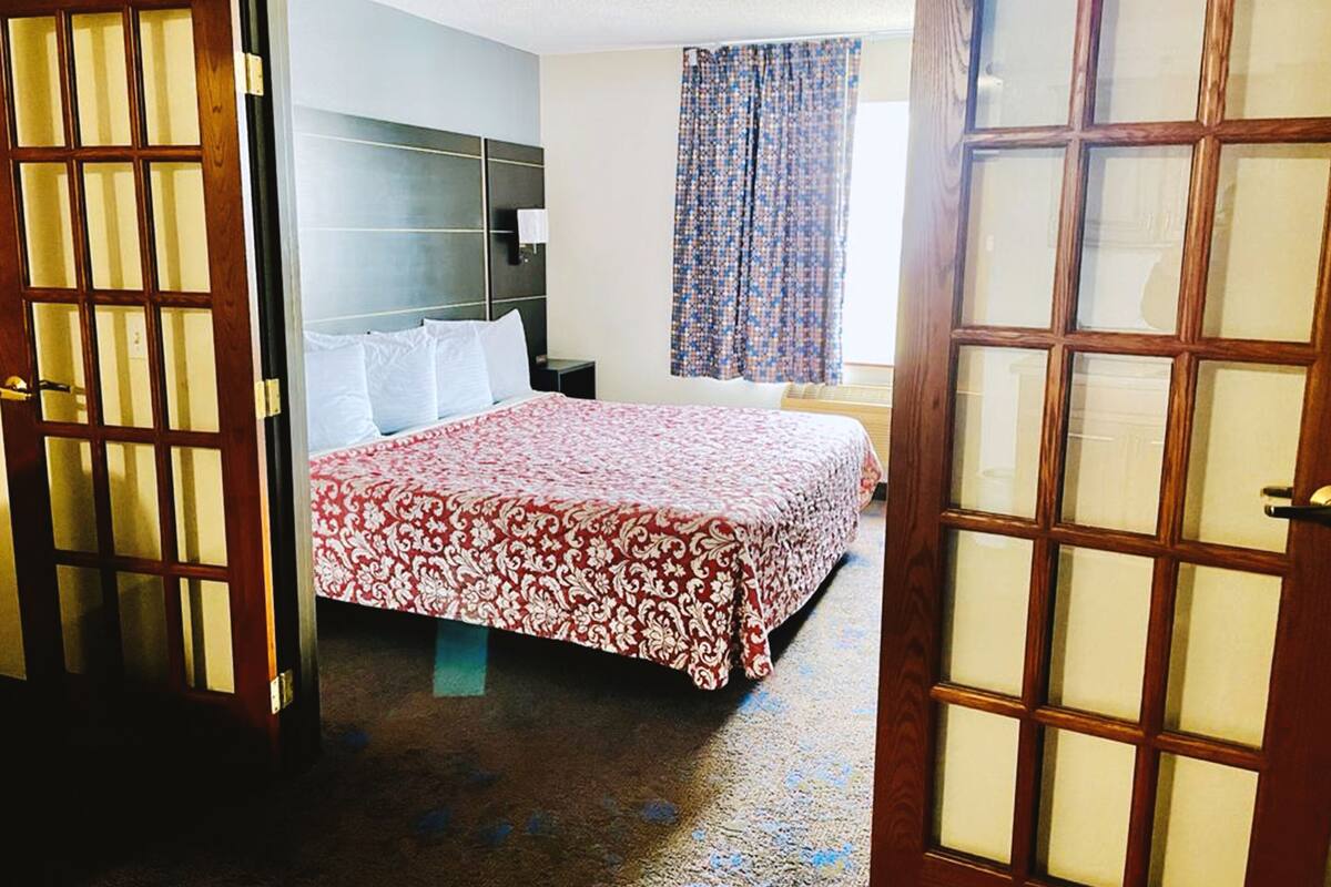 A hotel room with a bed, a nightstand, a headboard, and a window with curtains.