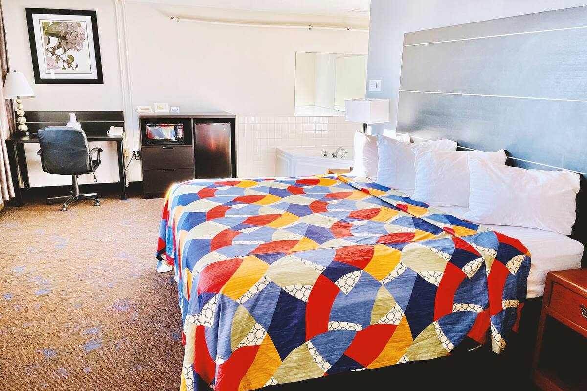 A hotel room with a bed, a desk, a chair, a TV, a bathroom, and a nightstand.