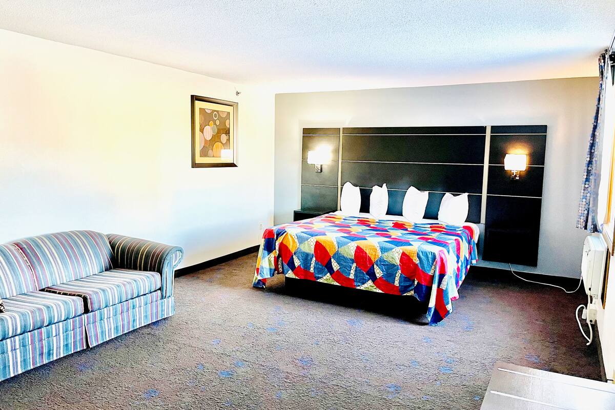 A hotel room with a bed, a sofa, a wall-mounted TV, and a painting.