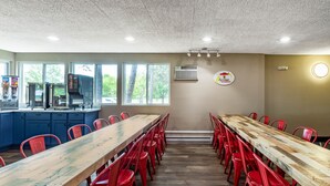 A long dining table with red chairs, a kitchen area with a coffee machine, and a view of trees through large windows. - Super 8 by Wyndham Duluth (Duluth)