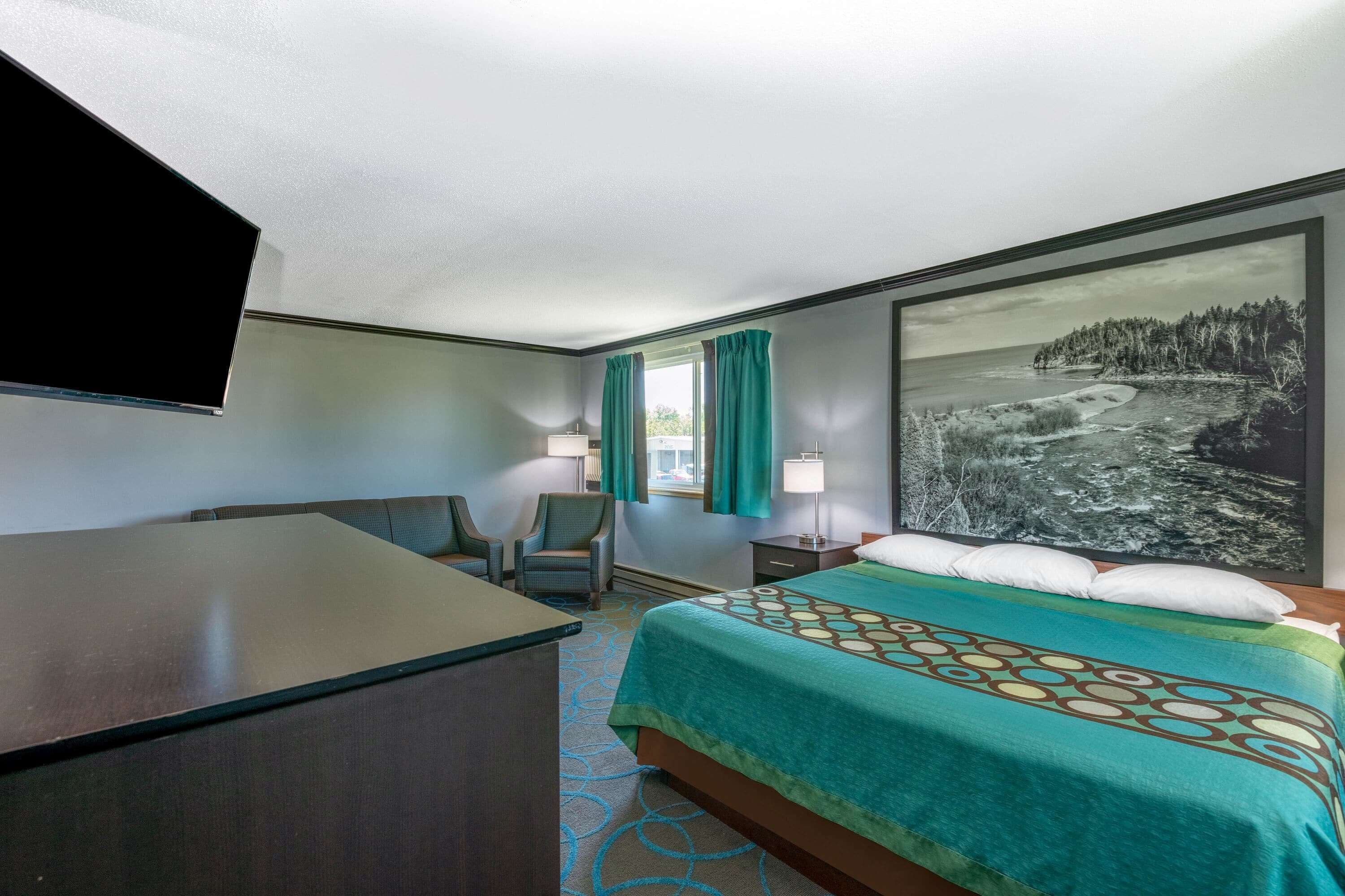 A hotel room with a bed, desk, chair, and a large window with curtains.