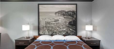 A hotel room with a large bed, two bedside tables with lamps, and a large framed picture of a coastal landscape.