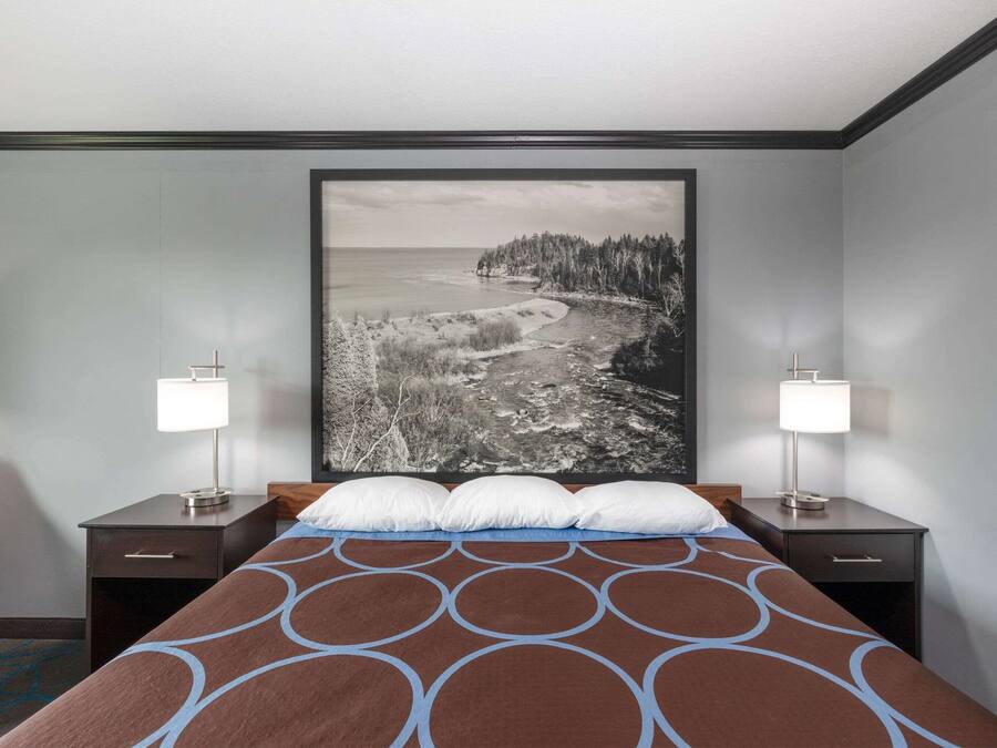 Habitación de hotel con una cama grande, dos mesitas de noche con lámparas, y un cuadro grande de un paisaje costero.