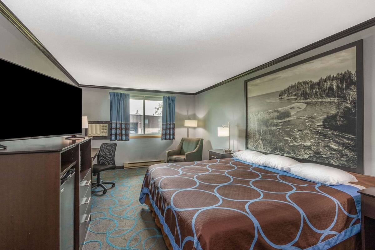 A hotel room with a bed, desk, chair, TV, and a large window with curtains.