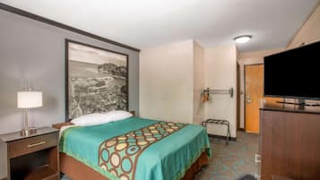 A hotel room with a bed, a television, a desk with a lamp, and a wall-mounted TV.