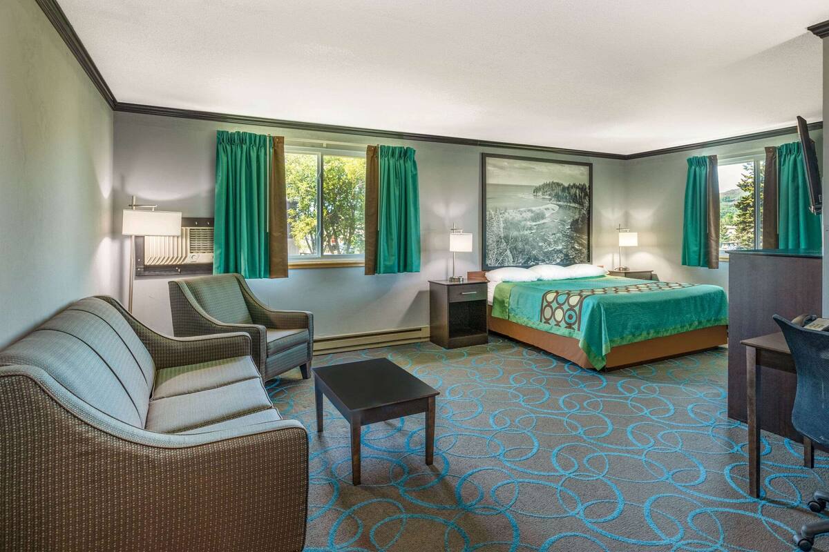 A hotel room with a bed, two chairs, a small table, and a desk.