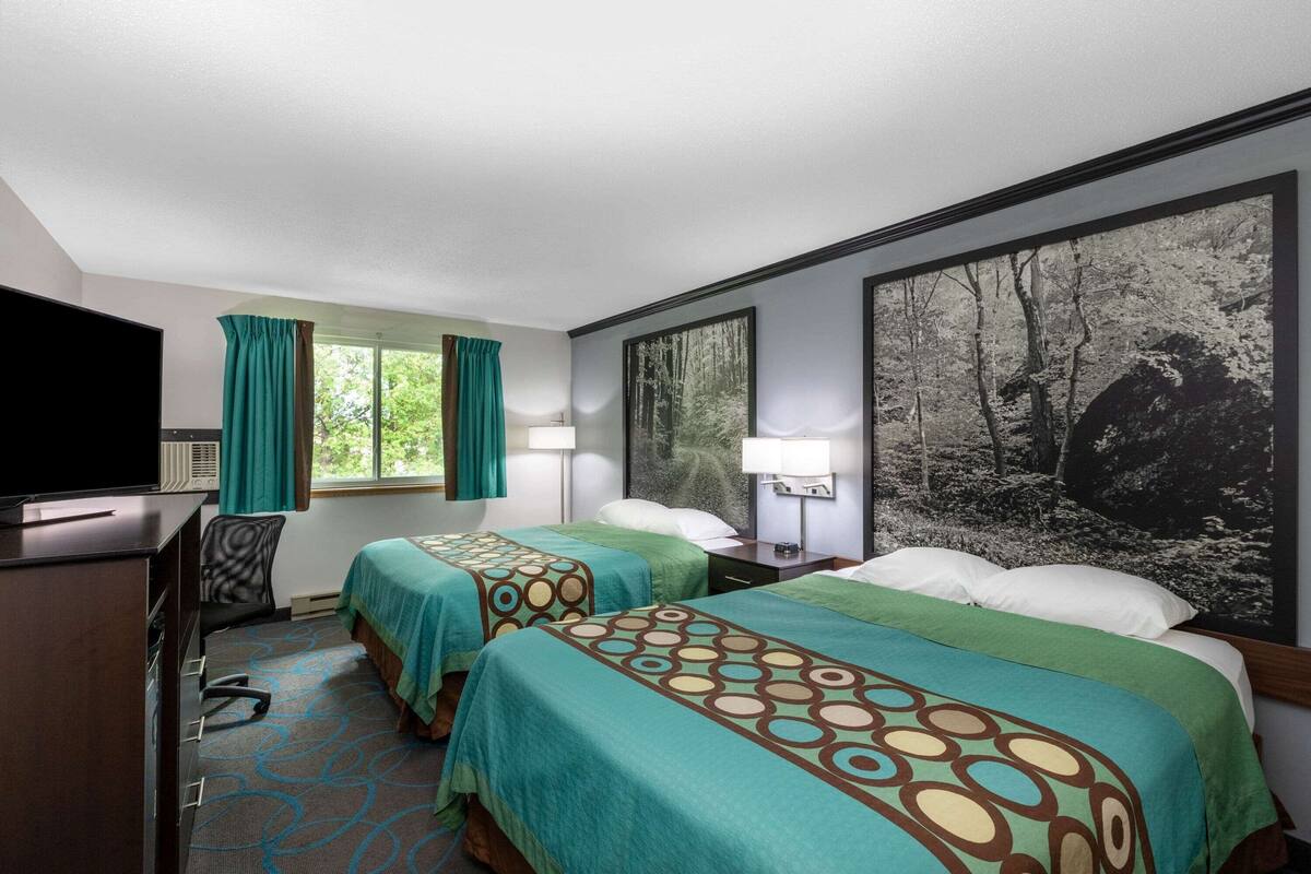 A hotel room with two beds, a desk, and a television.