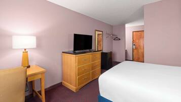 Habitación de hotel con cama, cómoda de madera, televisor, escritorio con lámpara y espejo.