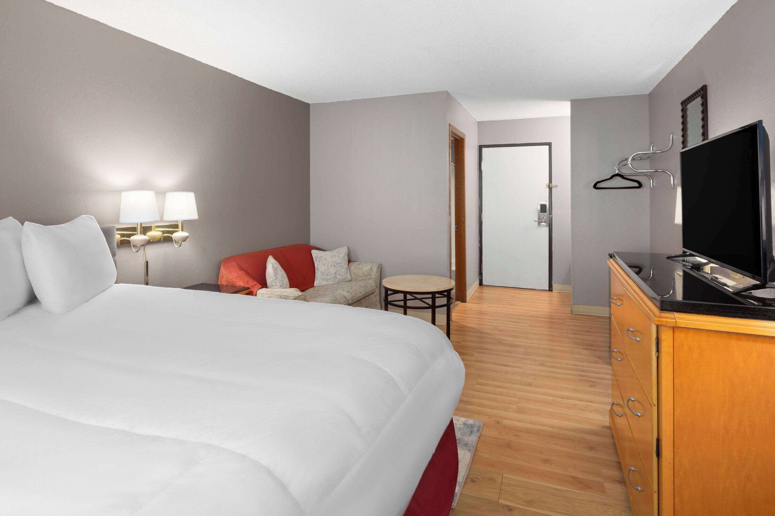 A hotel room with a large bed, a small sofa, a television, and a desk with a chair.