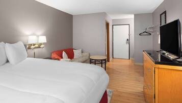 A hotel room with a large bed, a small sofa, a television, and a desk with a chair.