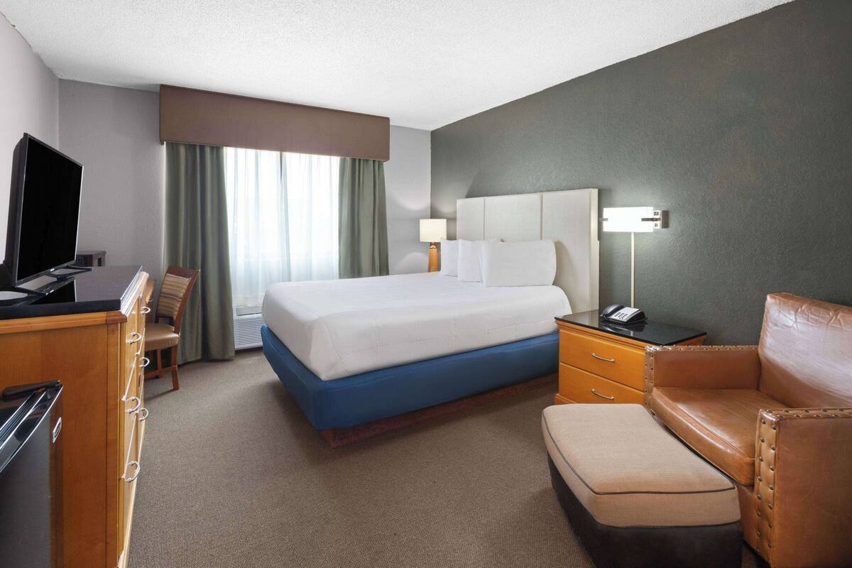 A hotel room with a bed, a desk with a TV, a desk lamp, a chair, and a sofa.