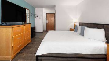 Quarto de hotel com uma cama grande, cómoda de madeira, televisão de ecrã plano e uma porta ao fundo.