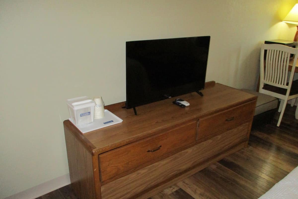 A wooden dresser with a flat-screen TV, a remote control, and a small white object on top.