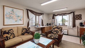 A furnished living room with a sofa, armchairs, a coffee table, and a dining table. There is a painting on the wall, a refrigerator, and a window with curtains. - Travelodge by Wyndham Redwood Falls (Redwood Falls)