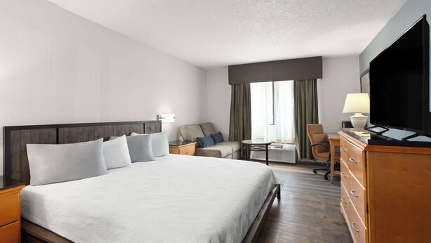 A hotel room with a large bed, a sofa, a desk, a TV, and a dresser. - Travelodge by Wyndham Redwood Falls (Redwood Falls)